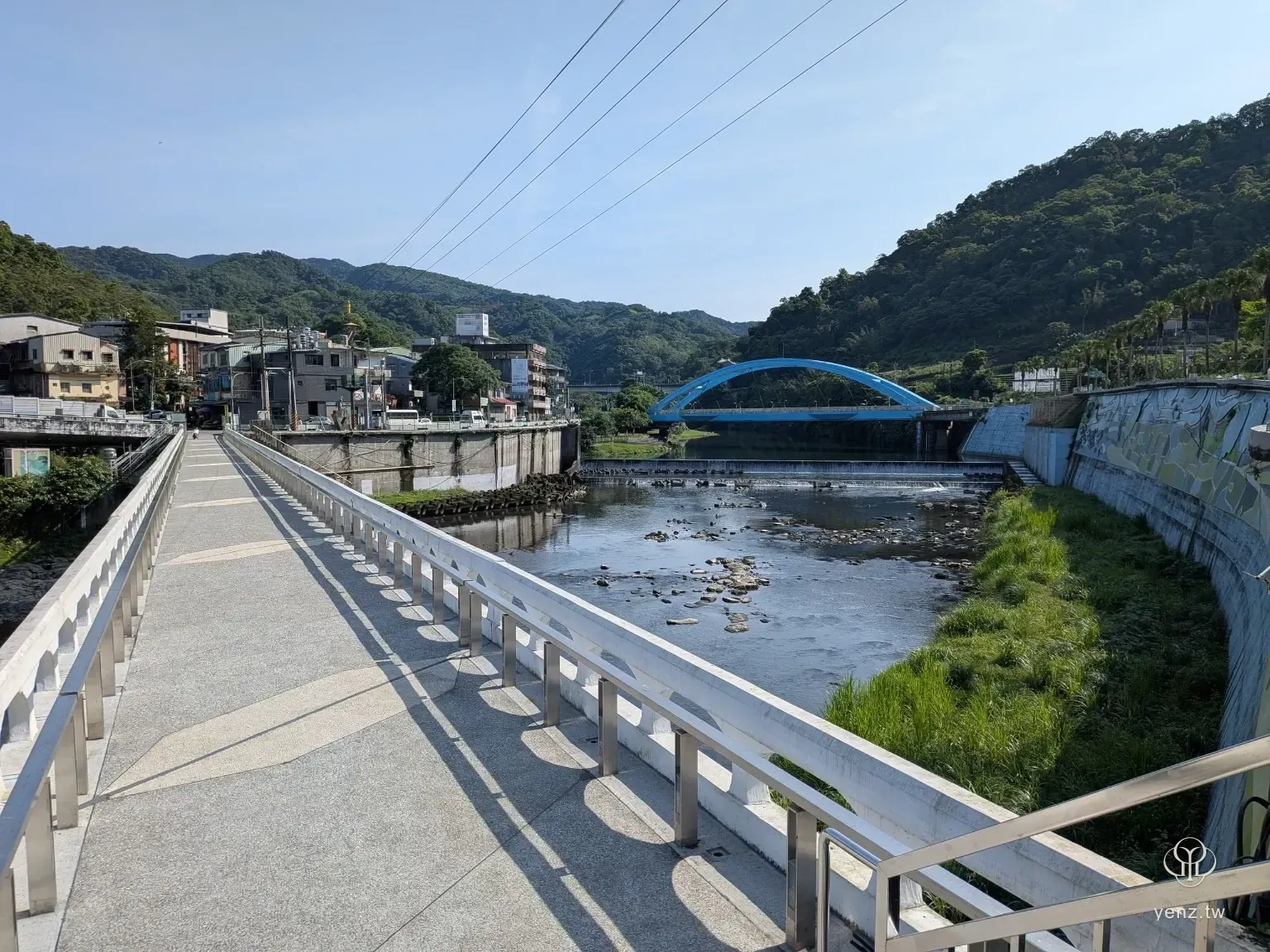 白色人行橋、藍色拱橋、溪流與坪林山景構成開闊視角。