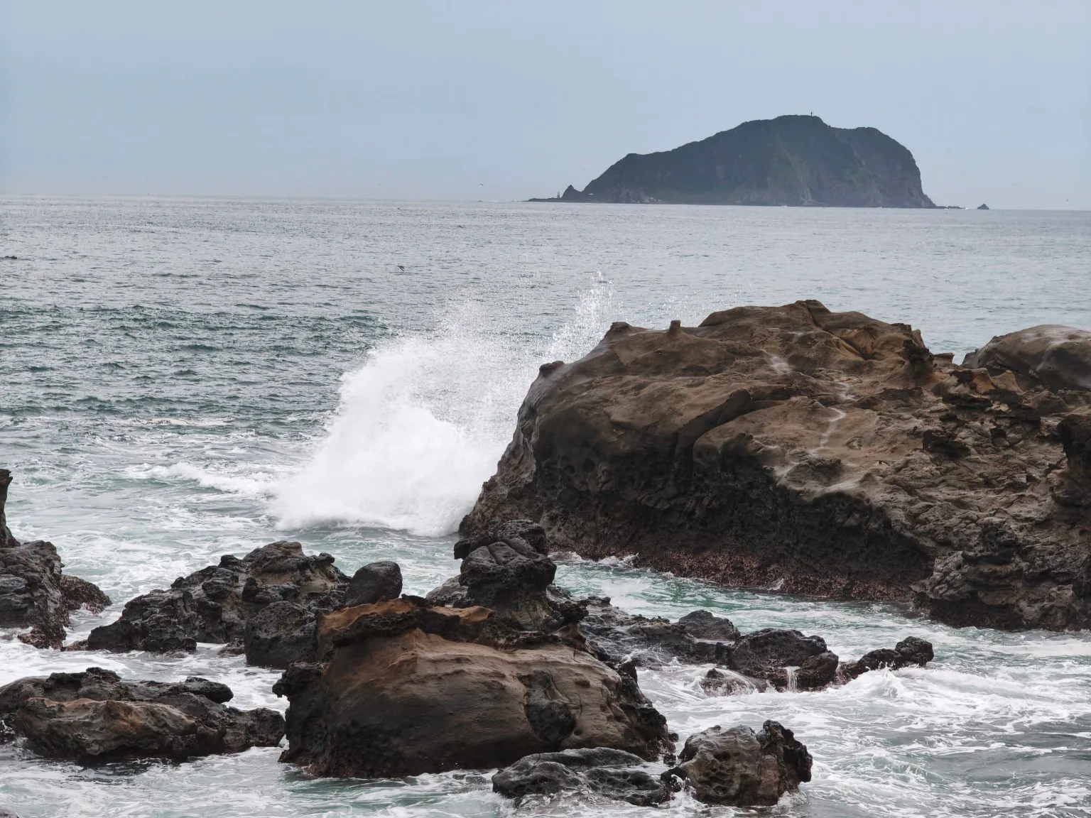 浪花拍打深澳海岸礁岩，遠方海面上可見基隆嶼。