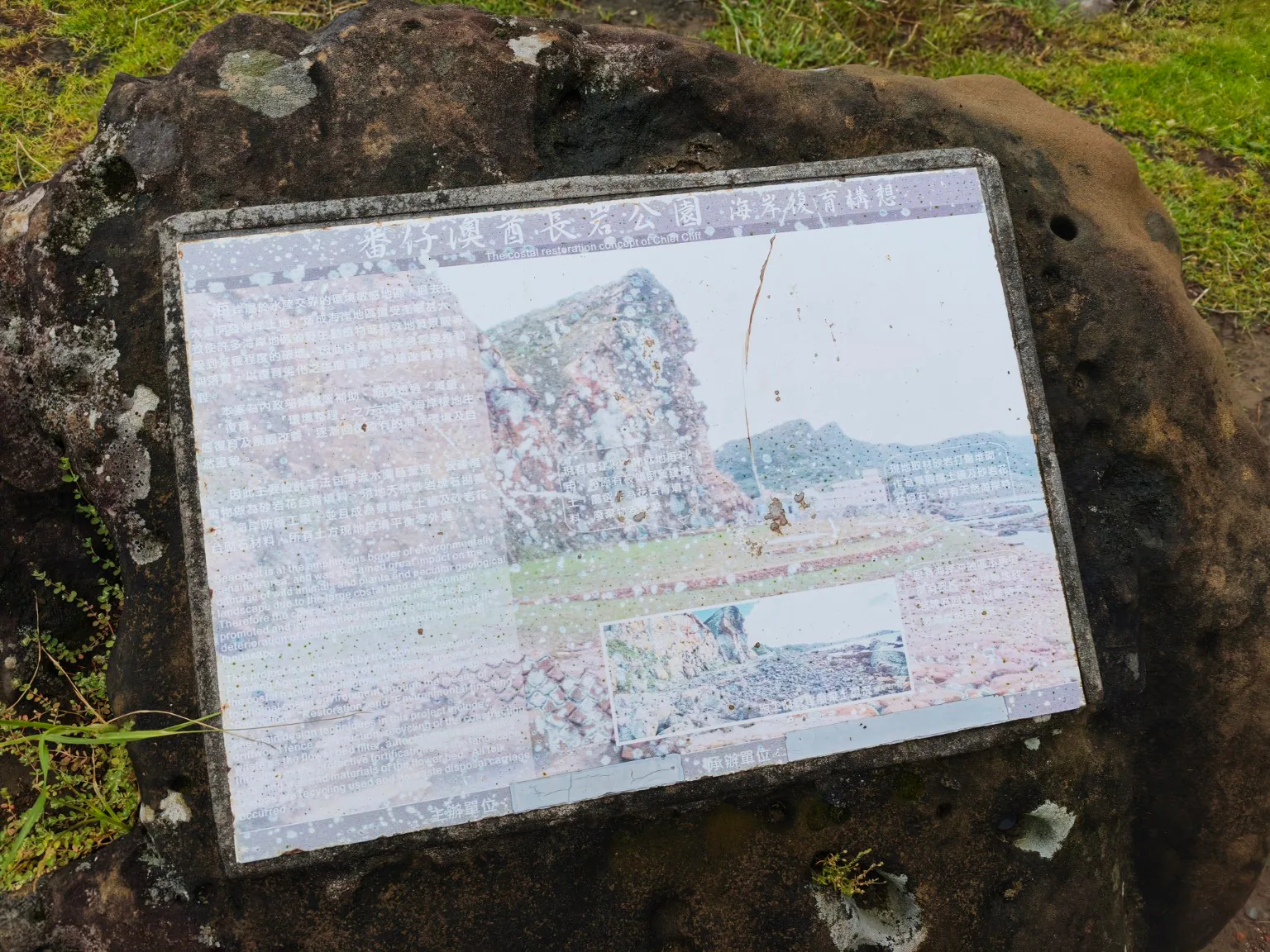 嵌在天然岩石中的蕃仔澳酋長岩公園海岸復育構想解說牌，文字與圖面已明顯褪色斑駁。