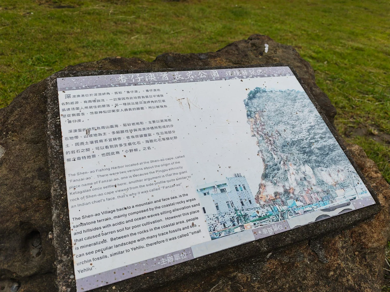嵌在天然岩石中的蕃仔澳酋長岩公園環境解說牌，介紹地名、砂岩地形與海岸化石。