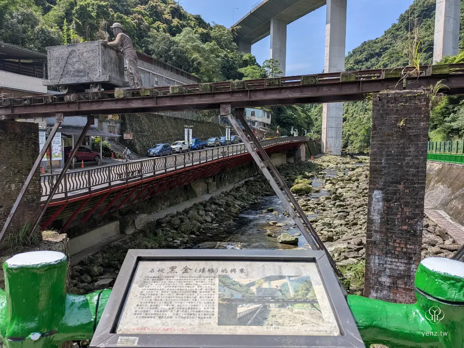 黑金解說牌、礦車與溪流同框，呈現石碇煤礦記憶。