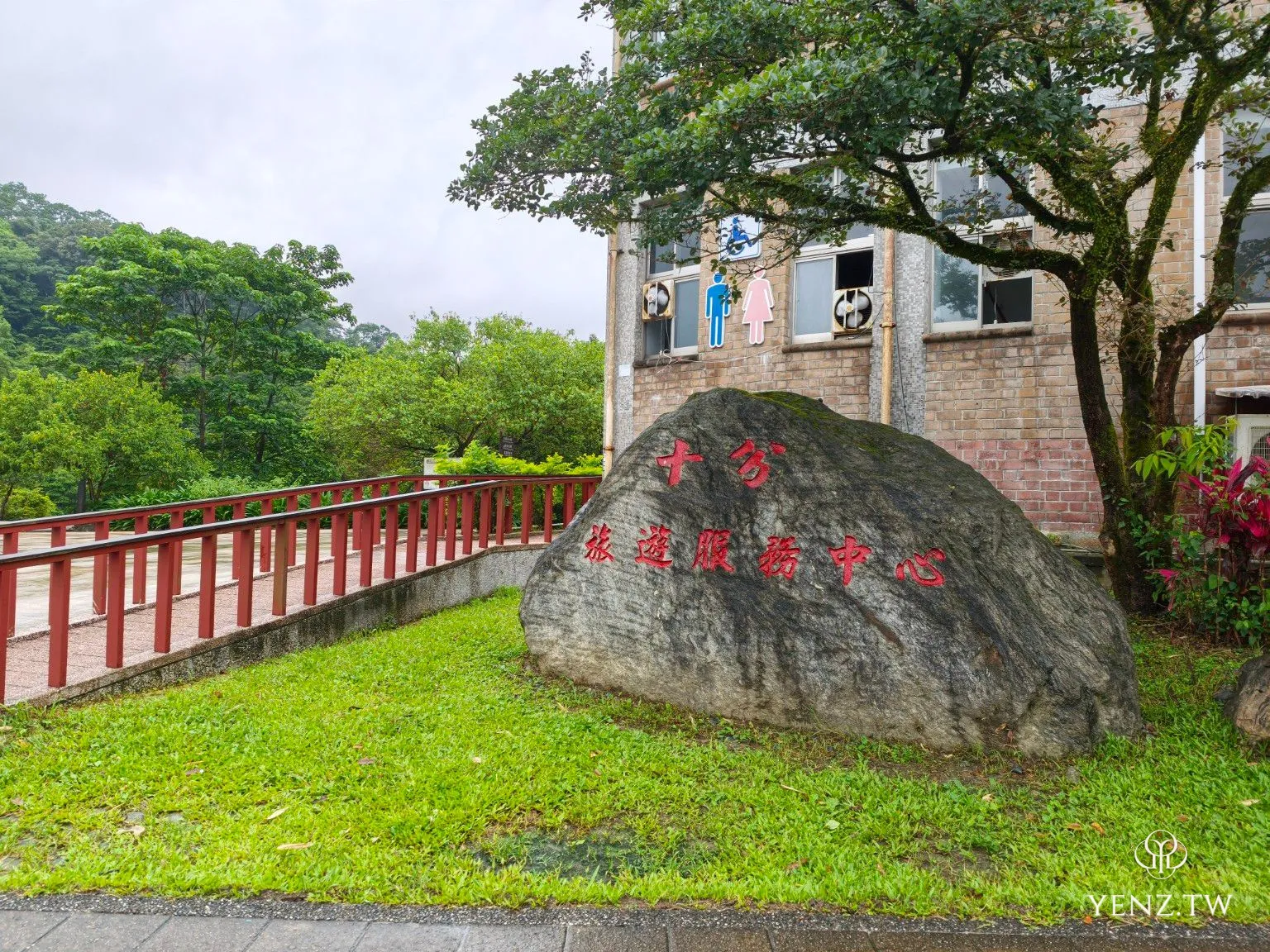 十分旅遊服務中心的入口石與雨後草地、紅色欄杆。